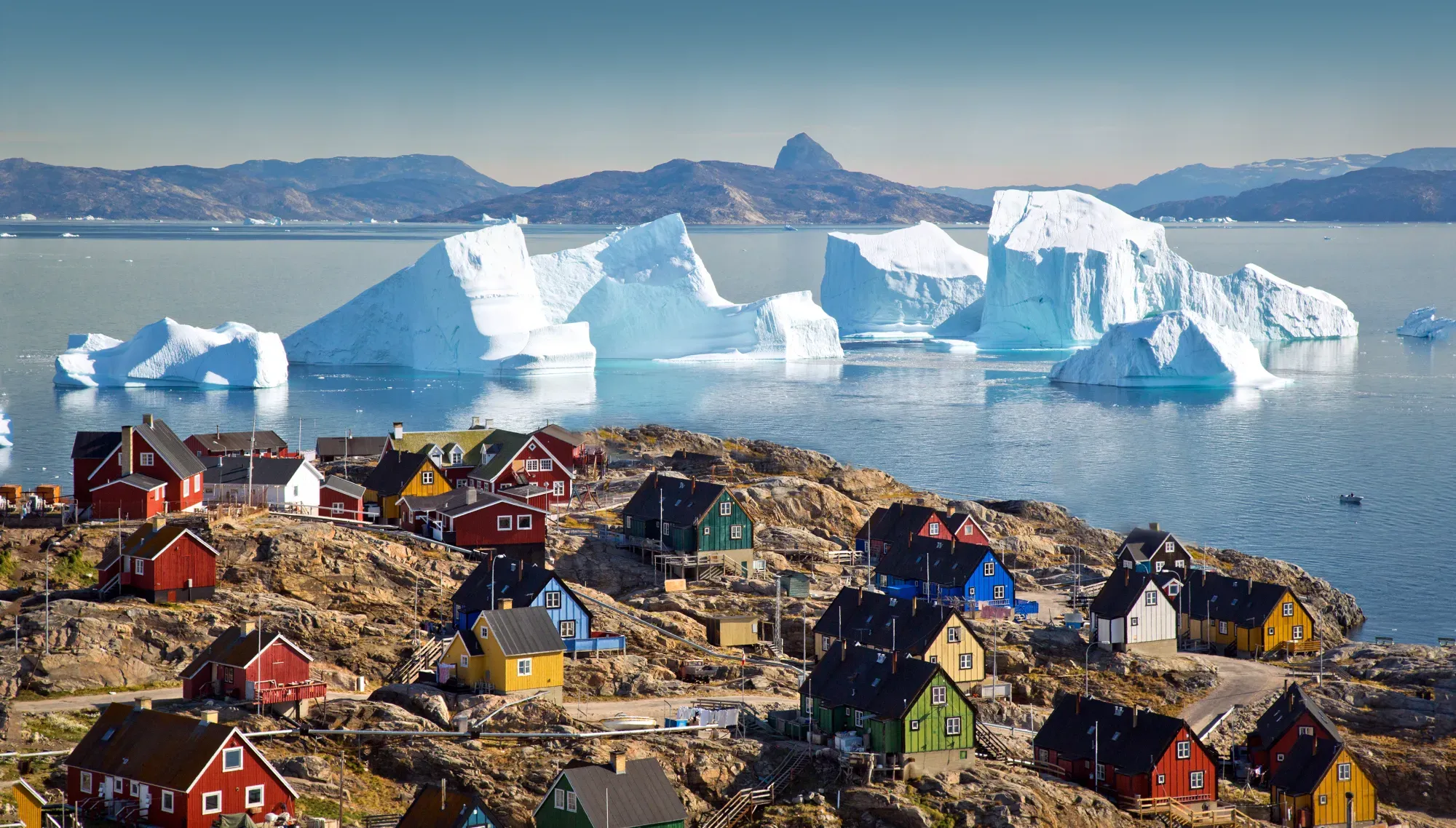 Brightly painted wooden houses on a rocky shore, huge icebergs in the bay beyond