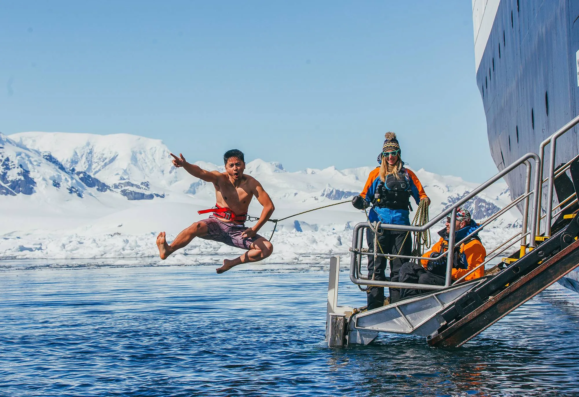 A guest leaps from the ship gangway into icy water on a safety line, crew watching