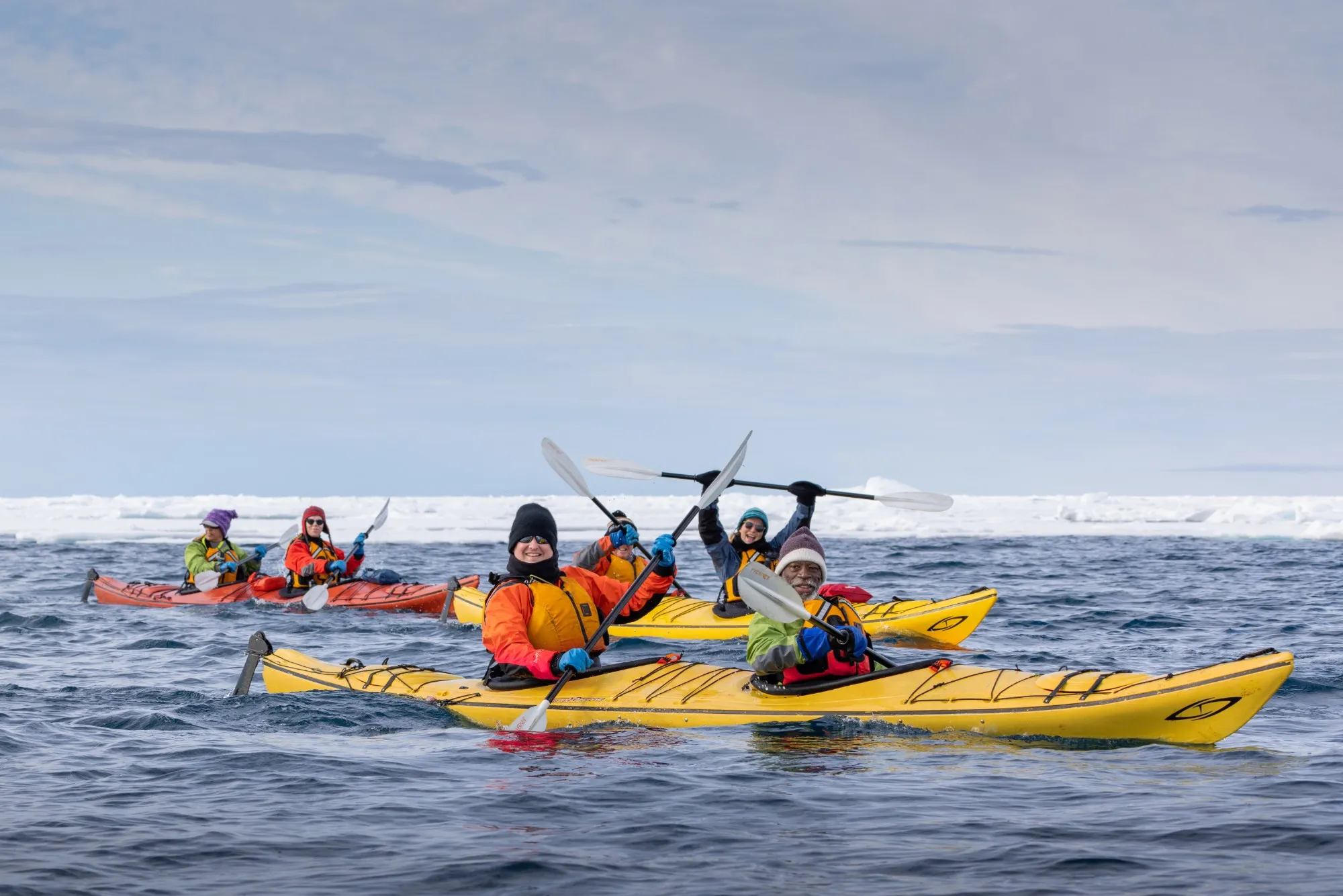Guests in yellow sea kayaks raising their paddles near the ice edge