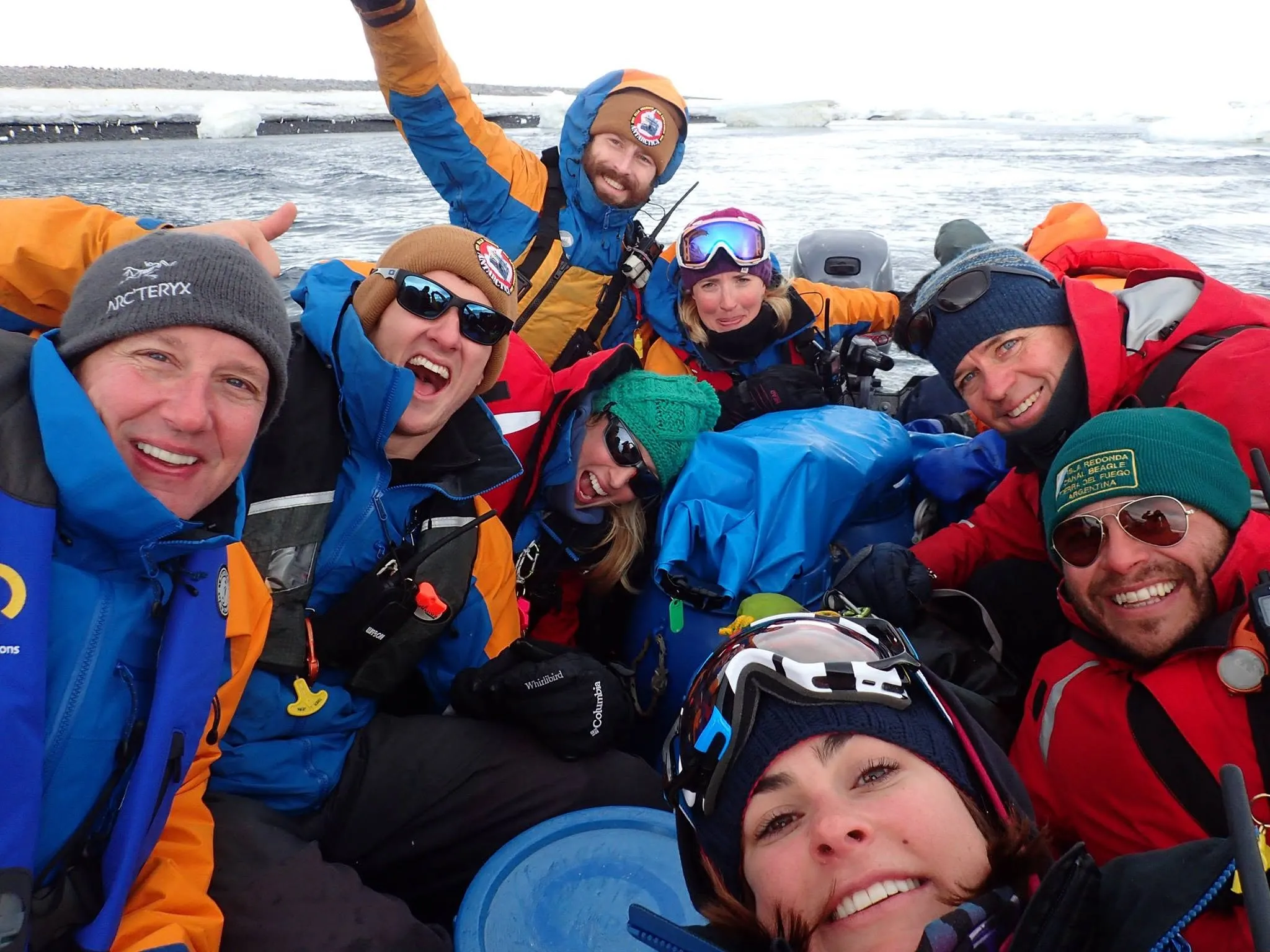 A Zodiac crowded with smiling people in expedition jackets, beanies and sunglasses squeezing in for a selfie, with sea ice behind them